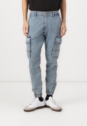 Jasnoniebieskie spodnie cargo z denimu, z wieloma kieszeniami bocznymi, luźnym krojem i elastycznymi mankietami przy kostkach.
