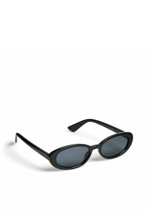 Zwarte ovale zonnebril met donker getinte glazen en slanke pootjes, rustend op een witte ondergrond.