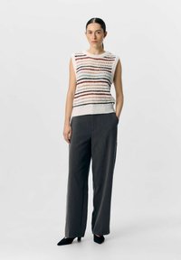 Haut sans manches en tricot avec des rayures horizontales multicolores ; associé à un pantalon large taille haute gris et des talons aiguilles noirs.