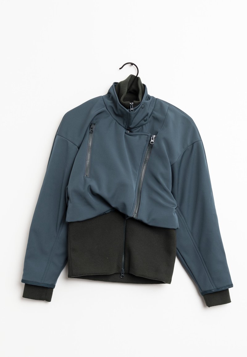 Mörk teal jacka med hög krage, med två dragkedjeförsedda bröstfickor och svarta axlar och muddar. Slätt, flexibelt material.