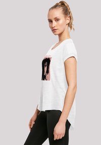 White cotton T-shirt with short rolled sleeves, featuring a pink box graphic of a person’s face. Hem is longer at the back.