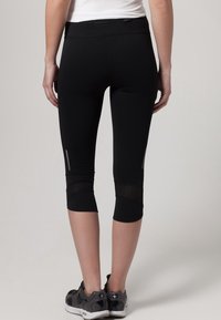 Leggings capri neri con vita alta, pannelli in rete nella parte inferiore delle gambe e dettagli riflettenti per una maggiore visibilità. Tessuto liscio ed elastico.