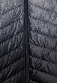 Sort pufferjakke med et kviltet chevronmønster, der har en central lynlås og en let metallisk glans. Blød tekstur.