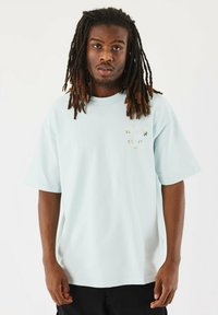 Camiseta de manga corta en azul claro, hecha de un tejido suave, con un pequeño logotipo impreso en la parte izquierda del pecho y un corte relajado.