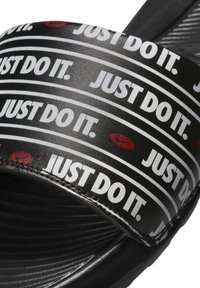 Sandale noire à glissière avec une sangle texturée portant le texte blanc "JUST DO IT." sur des rayures noires et un accent de logo rouge sur la sangle.