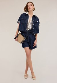 Chaqueta vaquera corta con bolsillos delanteros, camisa blanca con rayas azules, pantalones cortos a medida y bolso beige. Bailarinas nude de punta.