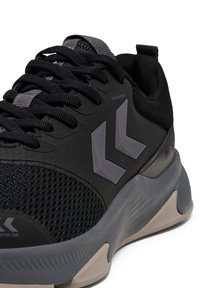 Zwarte sportieve schoenen met een mesh bovenkant, platte veters, grijze accenten en een gestructureerde zool met een opvallend rubberen patroon.