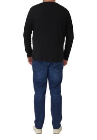 Schwarzes Langarmshirt aus Baumwollmaterial, Rundhalsausschnitt, kombiniert mit blauen Jeans, lockere Passform, schlichtes Design, Rückansicht dargestellt.