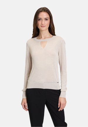 Pull en tricot beige clair avec un décolleté en forme de clé, des manches longues, des poignets côtelés et un ourlet ajusté. Agrémenté d'un petit logo.