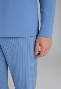 Top lungo a maniche blu chiaro abbinato a pantaloni a righe blu chiaro, caratterizzati da una texture liscia e un design aderente.