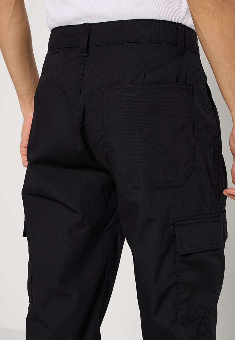 Pantalons cargo noirs avec une coupe décontractée, dotés de multiples poches, d'un tissu résistant et de détails de couture visibles sur la ceinture et les poches arrière.