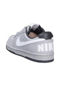 Sneaker grigio in pelle con un accento sul tallone nero, logo swoosh bianco, linguetta imbottita e suola in gomma testurizzata. Logo "NIKE" prominente sul tallone.
