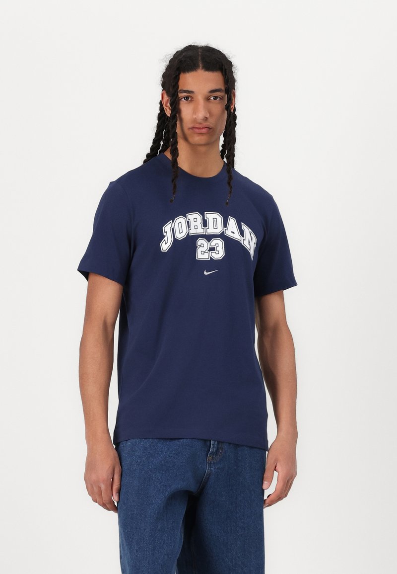 Námořnická modrá bavlněná trička s bílým nápisem "JORDAN 23" a logem Nike. Krátké rukávy, kulatý výstřih a volný střih. Džínové šortky.