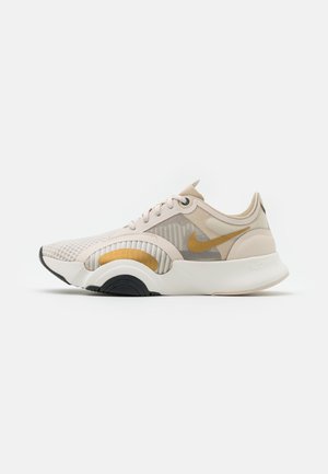 Beżowo-białe buty do biegania Nike z żółtym logo swoosh, siateczkową cholewką oraz grubą, białą, zakrzywioną podeszwą z czarnymi i żółtymi akcentami.