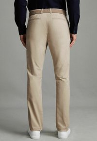 Chinos beiges en coton, avec une texture lisse, une coupe ajustée et une ceinture tressée. Associés à des baskets blanches.
