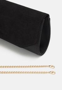 Black suede clutch with a smooth leather texture. Features a gold chain strap with clasps, folded design, and minimalistic aesthetics.