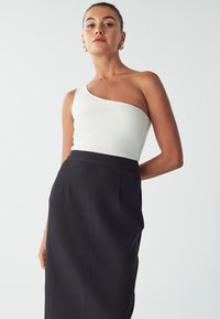 Haut blanc côtelé à une épaule associé à une jupe noire taille haute. Le haut présente une coupe ajustée, tandis que la jupe a une texture lisse.