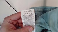 Lysblåt stof med en glat tekstur, der viser en plejeetiket med vaskeanvisninger og symboler, delvist synlig i en hånd.