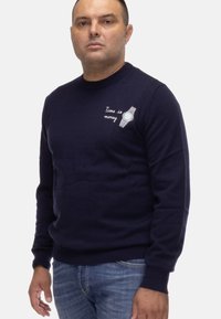 Maglione blu navy con scollo rotondo, caratterizzato da un design ricamato di un orologio e il testo "Il tempo è denaro." Texture morbida, vestibilità standard.