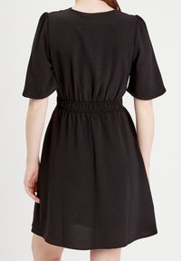 Robe noire à manches courtes, taille élastique et coupe décontractée. Tissu lisse avec une texture subtile. Coupe mi-longue.