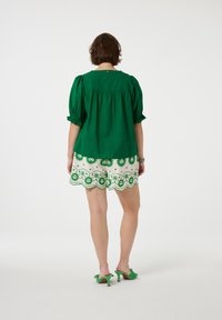 Groene blouse met pofmouwen gecombineerd met witte shorts met groene bloemenpatronen en een afgeronde zoom. Groene hakken maken de look compleet.