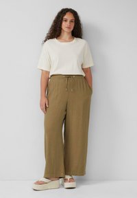 T-shirt crème à manches courtes, associé à un pantalon ample olive avec une taille à cordon et des poches latérales, porté avec des sandales à plateforme.
