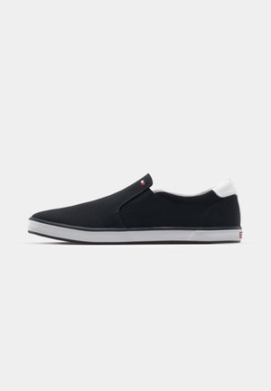 Black slip-on shoes with elastic side panels, white accents at the heel, and a textured rubber sole, featuring a minimalist design.
