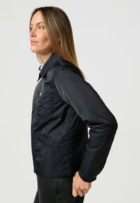 Schwarze Nylonjacke mit taillierter Passform, ausgestattet mit einem Frontreißverschluss, einer Brusttasche und detaillierter Nahtverarbeitung. Strukturiertem Stoff mit glatter Oberfläche.