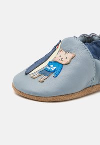 Helleblaue Lederschuhe mit einer Wildledersohle, versehen mit einem gestickten Katzendesign und einem blauen Shirt mit der Nummer 24 sowie einem gestreiften Akzent.