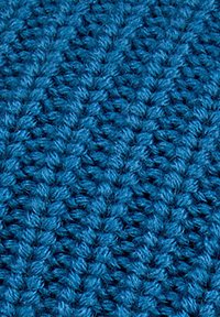 Primo piano di un tessuto blu a maglia testurizzato che mostra anelli di filato densi e intrecciati e motivi in rilievo tipici della lavorazione a maglia a mano.