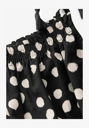 Tessuto nero con pois bianchi, dotato di una vita elasticizzata, texture arricciata e dettagli con frange sugli spallacci.