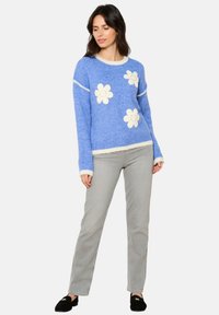 Vaaleansininen neulepaita, jossa valkoisia kukka-applikaatioita, pyöreä kaula-aukko sekä ribbireunat ja -hiha, yhdistettynä harmaisiin suoriin housuihin.