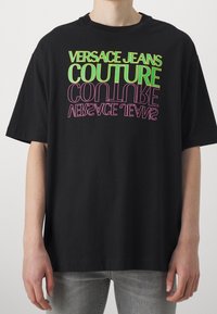 Svart bomull t-shirt med fet, flerfärgad text: "VERSACE JEANS COUTURE" i grönt och "CONTINUE" i rosa, med en lös passform.