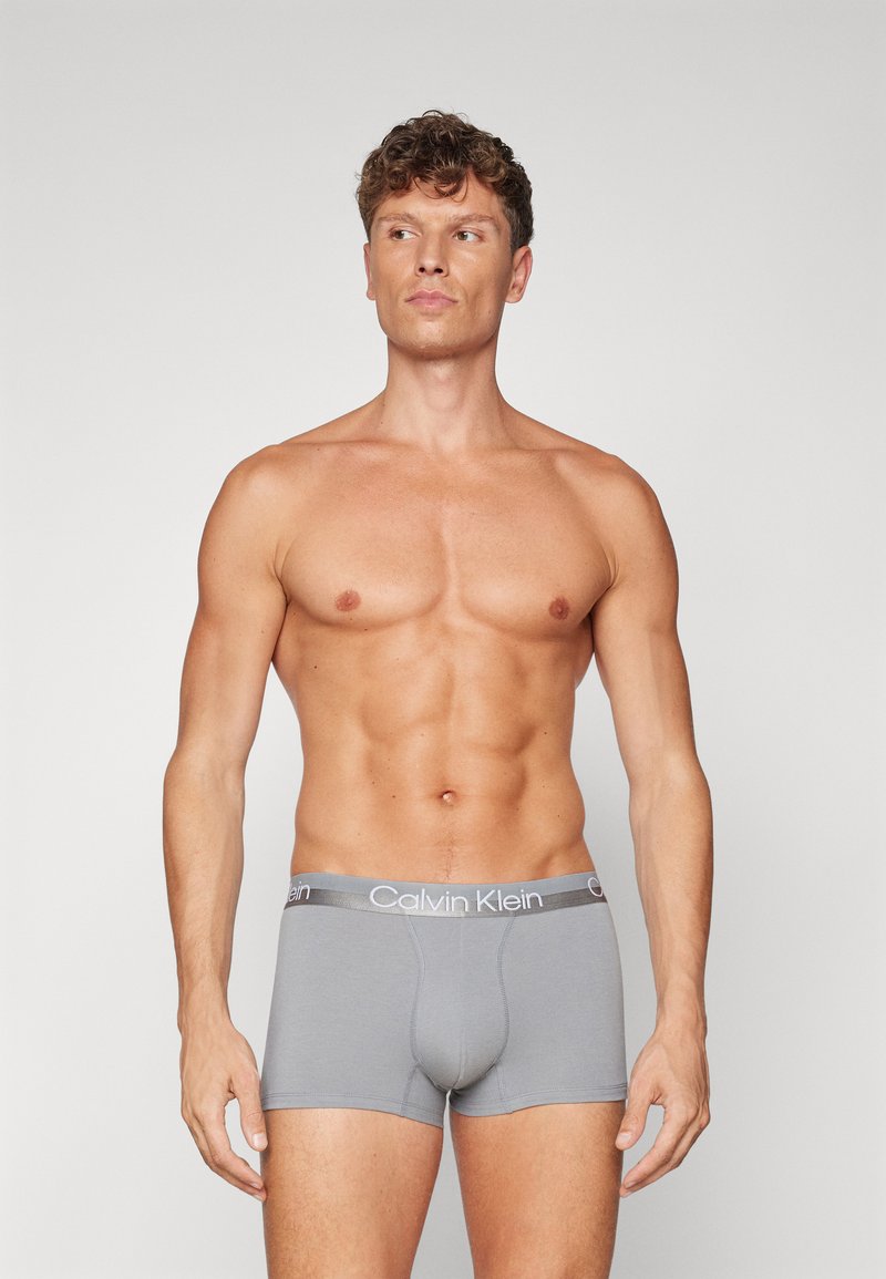 Pilkos boxer tipo kelnaitės su prigludusia forma, pagamintos iš medvilnės, turinčios lygią tekstūrą ir kontrastingą Calvin Klein logotipo juostą.