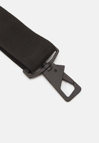 Fascia in nylon nero con superficie testurizzata e fibbia rettangolare in plastica dotata di un meccanismo di chiusura sicuro.