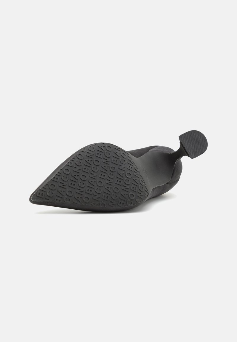 Schwarzer Schuh mit spitzem Zehenbereich, der aus weichem Obermaterial gefertigt ist. Er hat ein schlankes Design, eine strukturierte Gummisohle mit eingeprägtem Markenzeichen und eine kleine Lasche an der Rückseite.