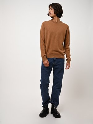Suéter de punto marrón, con cuello redondo, mangas largas, combinado con jeans de mezclilla azules y botas negras de tobillo. Textura suave, corte relajado.