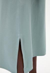 Hellgrünes Kleid mit seitlichem Schlitz, glatter Textur und sauberer Naht entlang dem Saum, das ein einfaches und modernes Design präsentiert.