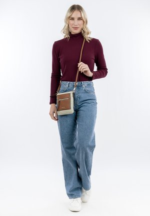 Borsa a tracolla con un corpo beige, dettagli marroni, una tasca con zip e una sottile tracolla regolabile. Indossata con jeans blu a vita alta e un top borgogna.