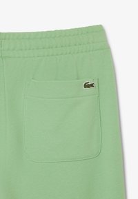 Groene katoenen sweatpants hebben een elastische tailleband, een achterzak en een klein geborduurd krokodillenlogo dicht bij de zak.