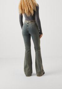 Höga flare-jeans i en urtvättad olivgrön denim, med dragkedja, knappstängning och bakfickor med subtil sömnad.