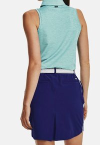 Bezrukávový, světle tyrkysový polo triko s límcem, v kombinaci s midi délky tmavě fialovými šortkami se stranovými pruhy a kapsami.