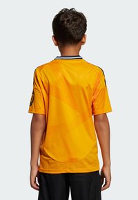 Maillot de sport jaune à manches courtes, avec un motif géométrique, un col bleu marine et des accents noirs contrastants sur les manches.