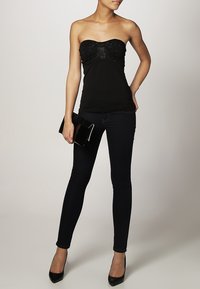 Haut noir sans bretelles avec un corsage texturé orné de strass, associé à un jean skinny foncé et des talons hauts noirs. Pochette noire tenue à la main.