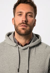 Sudadera gris con cordón, que presenta una textura suave. Una camisa de cuadros es visible debajo, con patrones en rojo y azul.