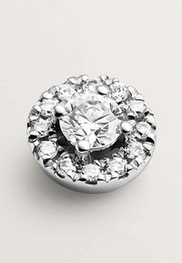 Una pieza de joyería de plata redonda con un diamante redondo central, rodeado de piedras claras más pequeñas en un engaste texturizado.