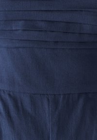 Granatowa tkanina z poziomymi fałdami i gładką strukturą, z prostym krojem i widocznymi detalami szycia.