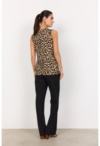Top sin mangas de estampado de leopardo, hecho de tela suave, combinado con pantalones negros de pierna recta y sandalias de tacón claro en color marrón.