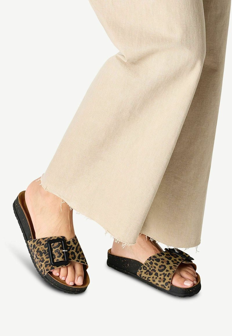 Luipaardprint slidersandalen met een zwarte gesp, voorzien van een zachte voetbed en zwarte gestructureerde buitenzool, gecombineerd met beige wijde broek.