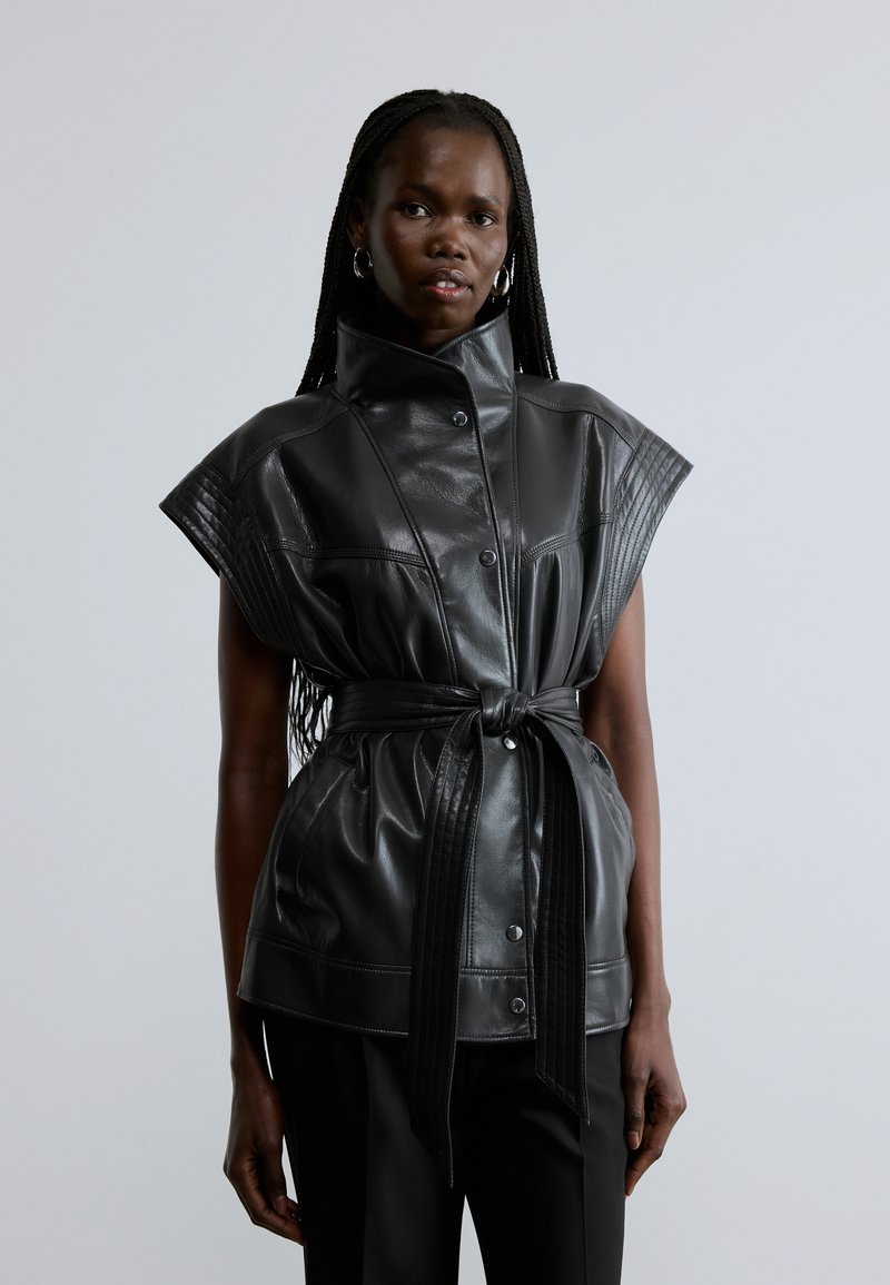 Mustast nahast vest kõrge krae, lühikeste varrukatega ja vöökohal vööga. Esiküljel on soonikkatted ja nööbid. Sile tekstuur.